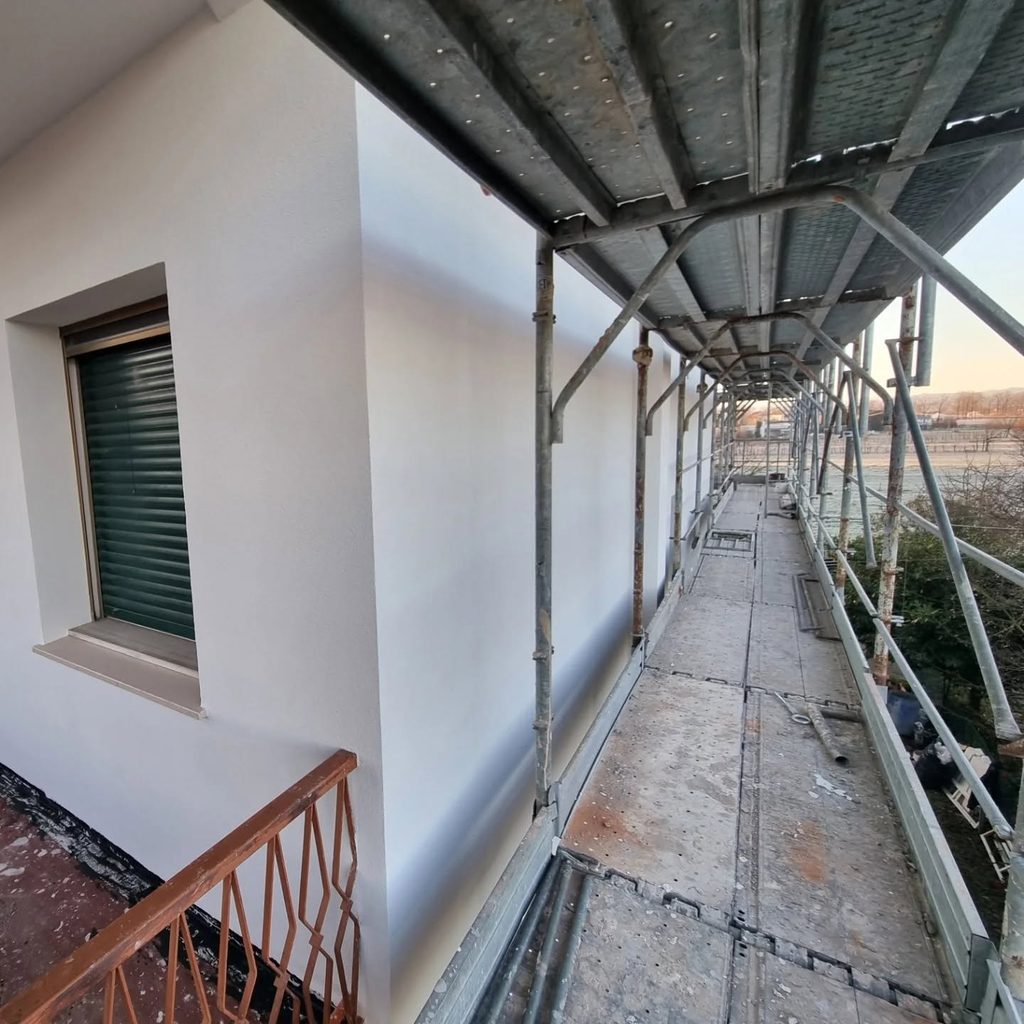 Facciata rasata a finitura bianca vista dal ponteggio, con linee pulite e spigoli definiti